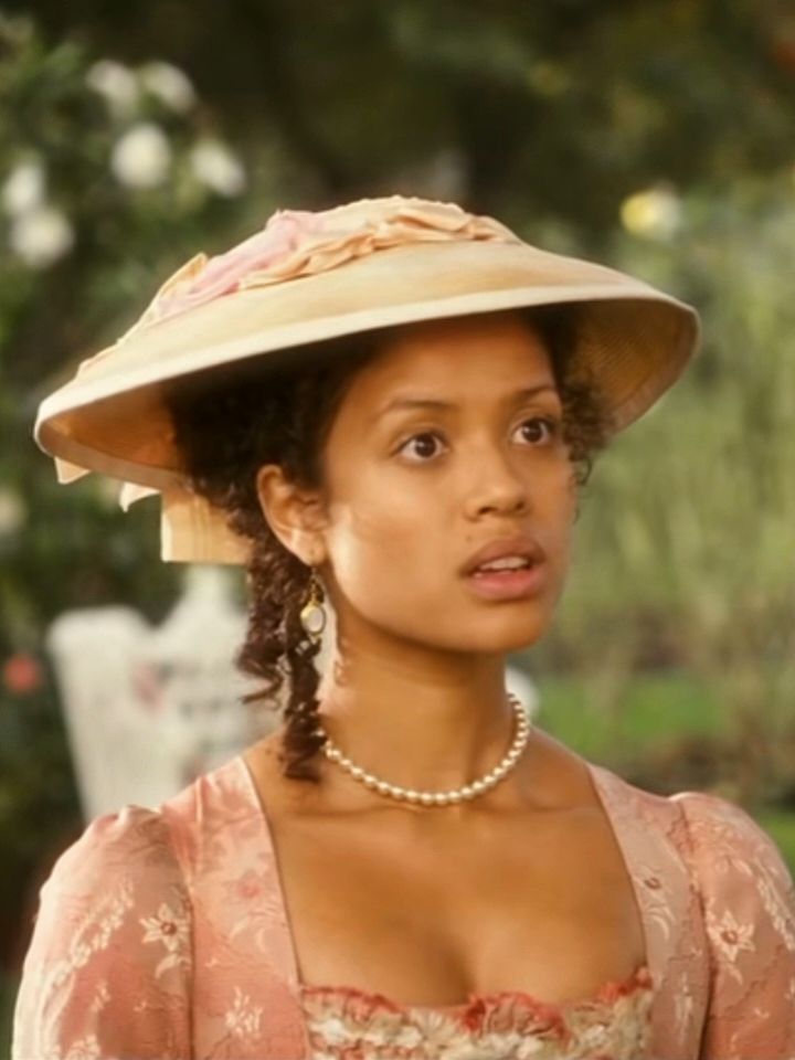 a woman in a pink dress and hat is looking at the camera while wearing pearls