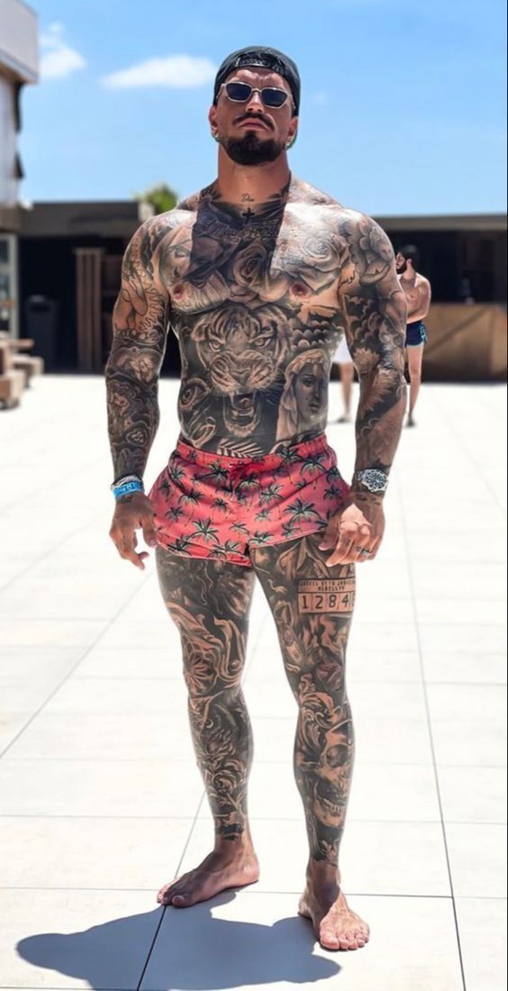 a man with tattoos on his body standing in front of a white tile floor and wearing sunglasses