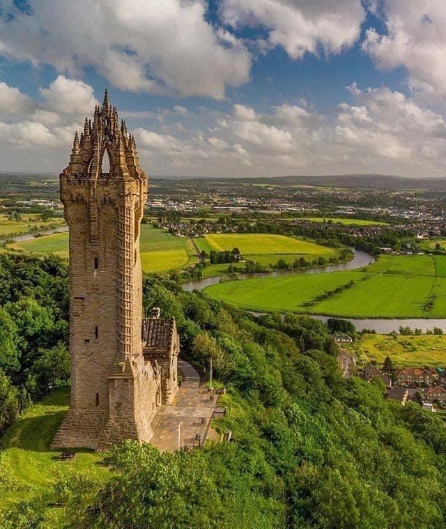 an aerial view of a tall tower in the middle of a lush green field and river