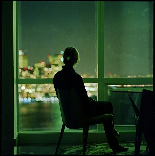 a person sitting in a chair looking out the window at city lights and skyscrapers