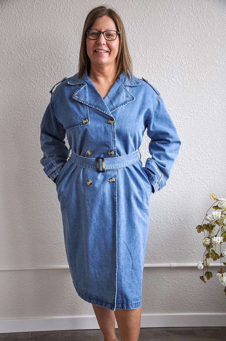 This medium denim trench coat exudes timeless elegance and casual sophistication. The medium denim wash gives it a classic yet contemporary look, while the waist belt detail adds a touch of tailored refinement, allowing for a customizable fit. With its long denim coat fit, this piece offers both warmth and style, making it a versatile addition to any wardrobe. The classic button closure and long sleeves provide a traditional trench coat silhouette, perfect for layering over various outfits. The Denim Outerwear With Belt Loops For Work, Long Sleeve Denim Outerwear With Belt Loops, Belted Denim Jacket For Workwear, Spring Denim Blue Belted Outerwear, Denim Blue Belted Outerwear For Spring, Denim Jacket With Belted Cuffs, Long Sleeve Denim Jacket With Belted Cuffs, Denim Outerwear With Double Button Closure In Medium Wash, Medium Wash Belted Outerwear For Work