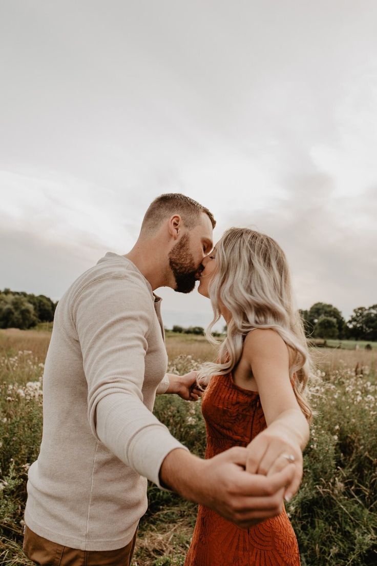 a man and woman standing in a field holding each other's hands as they kiss