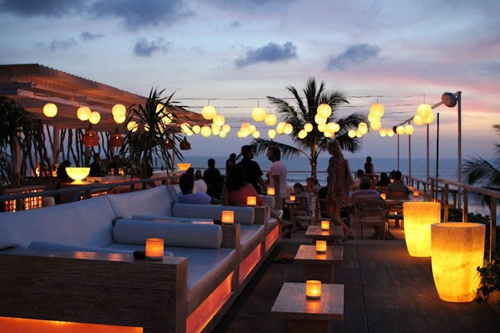 a group of people sitting on top of a wooden deck next to the ocean at night