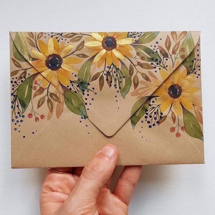 a hand holding an envelope with flowers painted on it