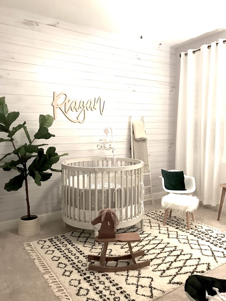 a baby's room with a crib, rocking chair and potted plant