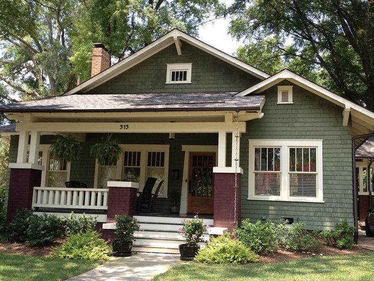 a green house with red shutters and white trim on the front porch, sitting under trees