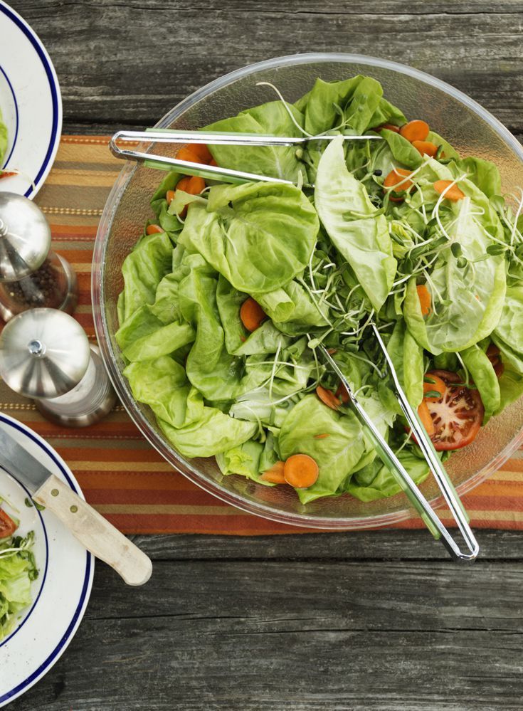 a salad with lettuce and carrots in a glass bowl on a table