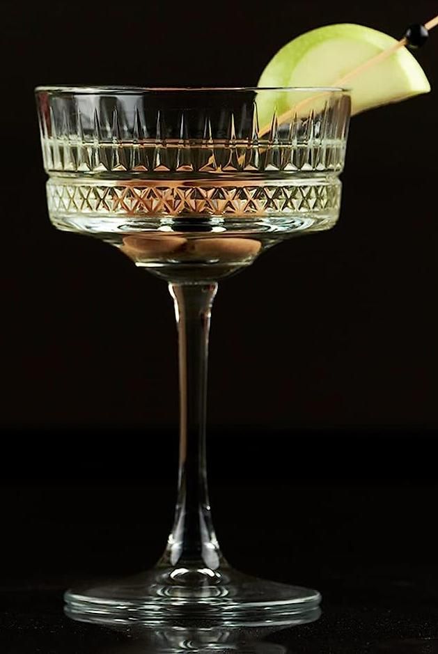 a martini glass with an apple on the rim and a garnish in it