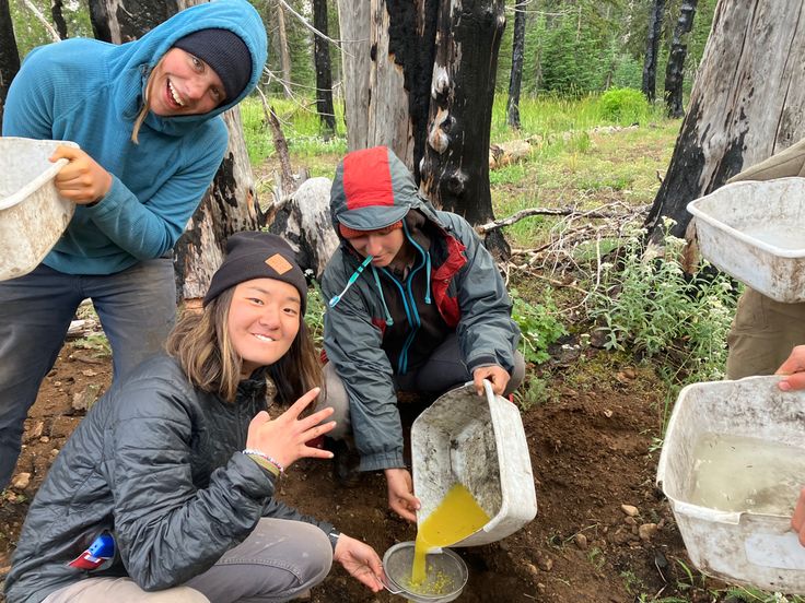 three people in the woods with buckets full of water and one person holding something