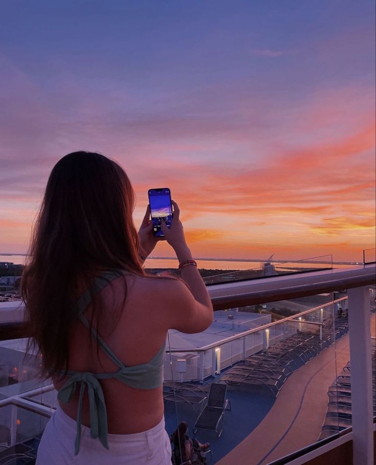 a woman standing on top of a balcony looking at the sky with a cell phone in her hand