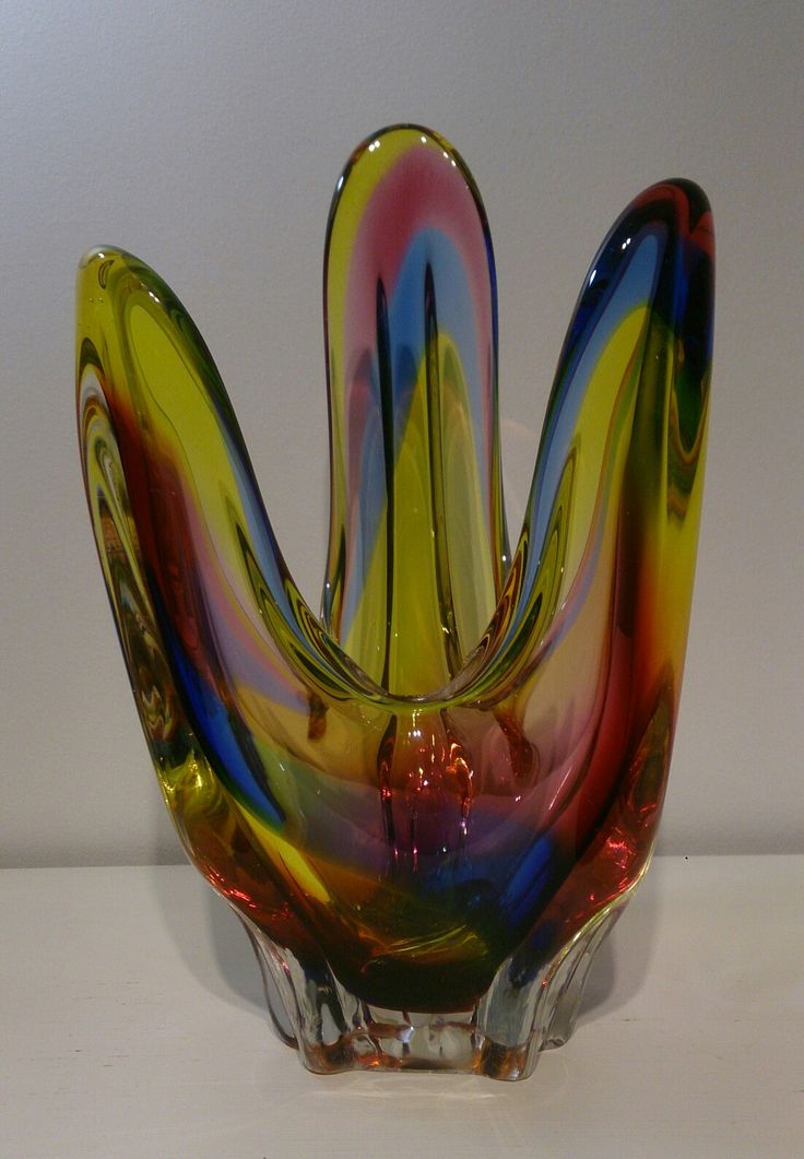 a multicolored glass vase sitting on top of a white table next to a wall