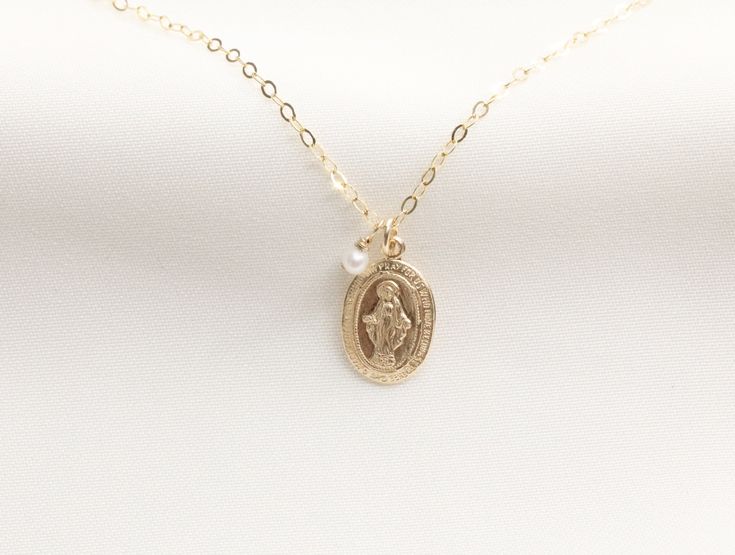 Tiny Virgin Mary with Pearl Necklace / Religious Necklace / Miraculous Medal / Baptism Necklace / Virgin Mary / 14k Gold Filled - 9 x 13mm Gold Filled Virgin Mary Pendant - Front design: Mama Mary - Back design: letter M with a cross on top and scattered stars - 3mm genuine freshwater pearls - Virgin Mary Charm (Left Side) Pearl (Right Side) AVAILABLE CHAIN + Round Flat Gold Filled AVAILABLE LENGTH + 16 inches Gold Filled + 17 inches Gold Filled + 18 inches Gold Filled - Pendant and Chain Materi 14k Gold Miraculous Medal Necklace For Anniversary, 14k Gold Necklace With Miraculous Medal For Anniversary, Personalized Yellow Gold Necklaces For First Communion, Personalized Yellow Gold Necklace For First Communion, Gold Jewelry For First Communion And Mother's Day, Personalized Gold Necklaces For Baptism, Personalized Gold Necklace For Baptism, 14k Gold Jewelry For First Communion, Gold Pendant Necklace For First Communion