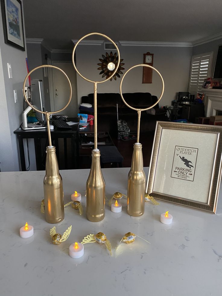 four gold vases with candles on a table in front of a picture frame and framed photograph