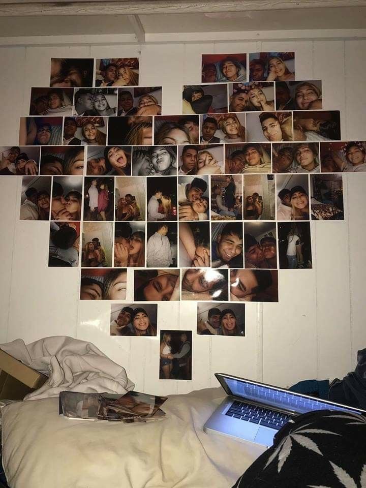 a wall with many pictures on it and a laptop in the foreground, next to a bed