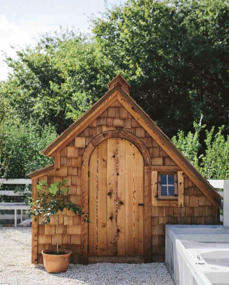 a small wooden building with a potted plant next to it and a white fence in the background