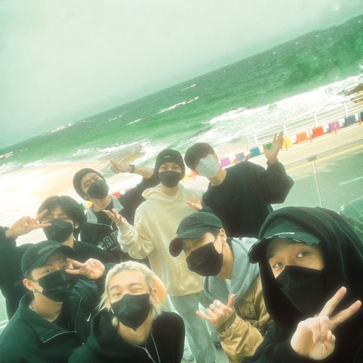 a group of young people standing next to each other near the ocean with their hands in the air