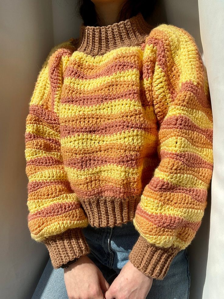 a woman wearing a yellow and brown sweater sitting on top of a white couch with her hands in her pockets