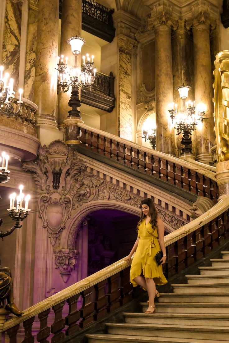 a woman in a yellow dress is walking down some stairs with chandeliers on either side