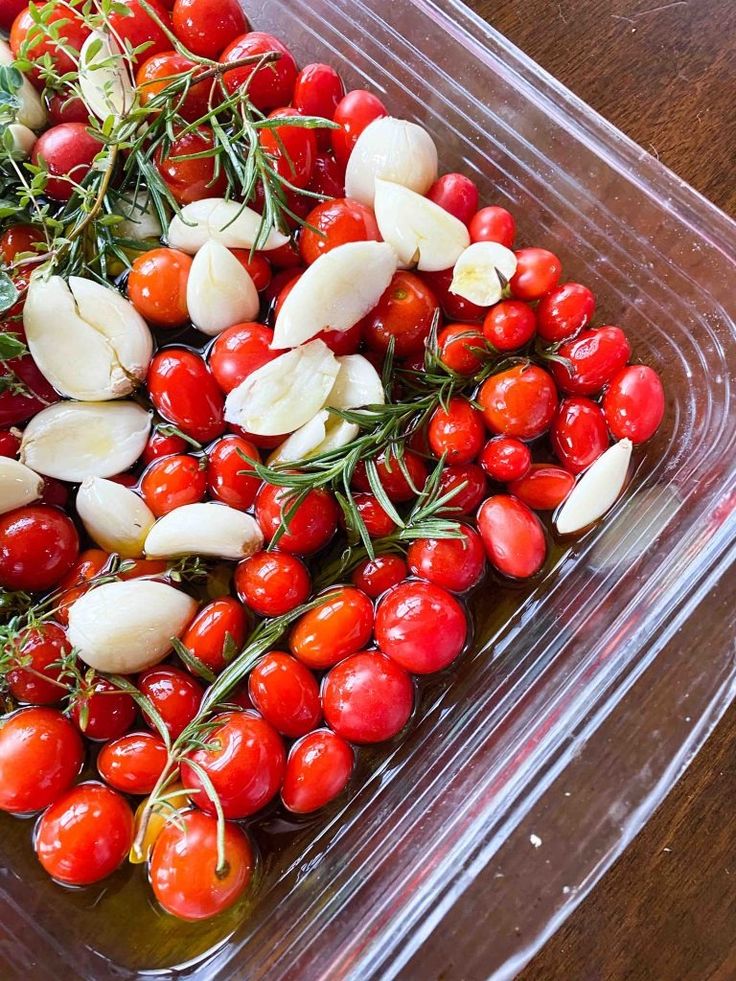 a plastic container filled with lots of cherry tomatoes and garlic on top of a wooden table