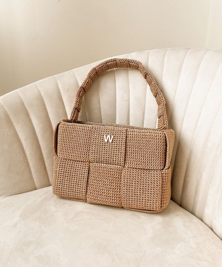 a wicker purse sitting on top of a white couch next to a wall with the letter w