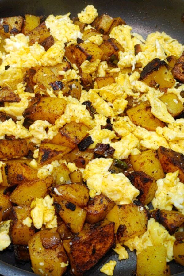 scrambled eggs and potatoes in a skillet ready to be cooked on the stove top