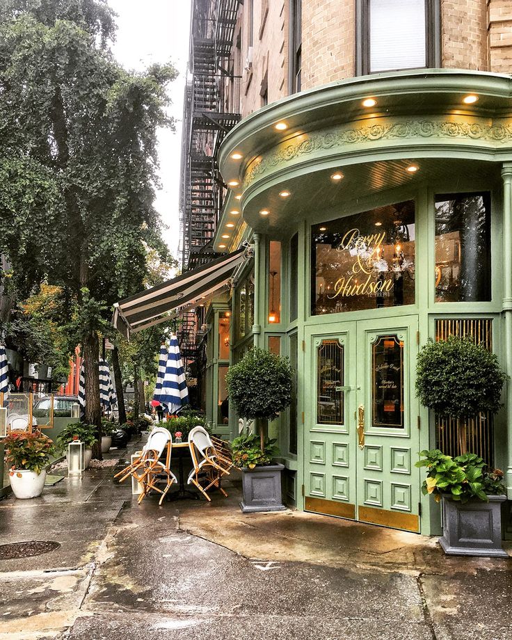 an outdoor cafe with potted plants and umbrellas on the sidewalk in front of it