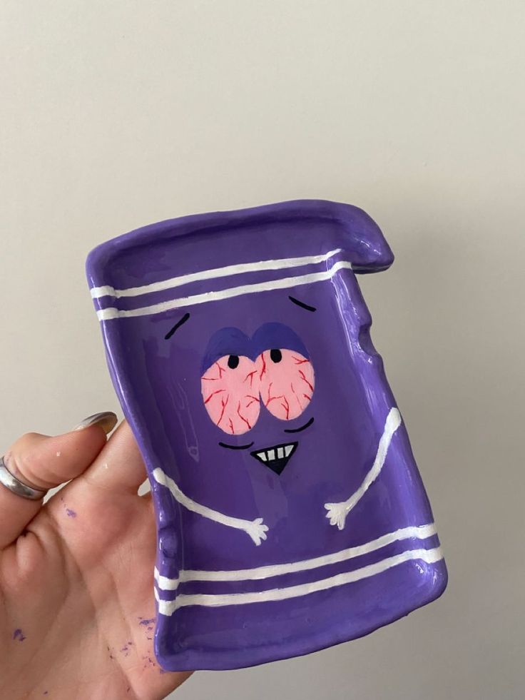 a hand holding a purple cup with two faces painted on it