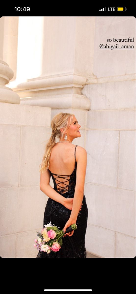 a woman in a black dress standing next to a white wall with flowers on it