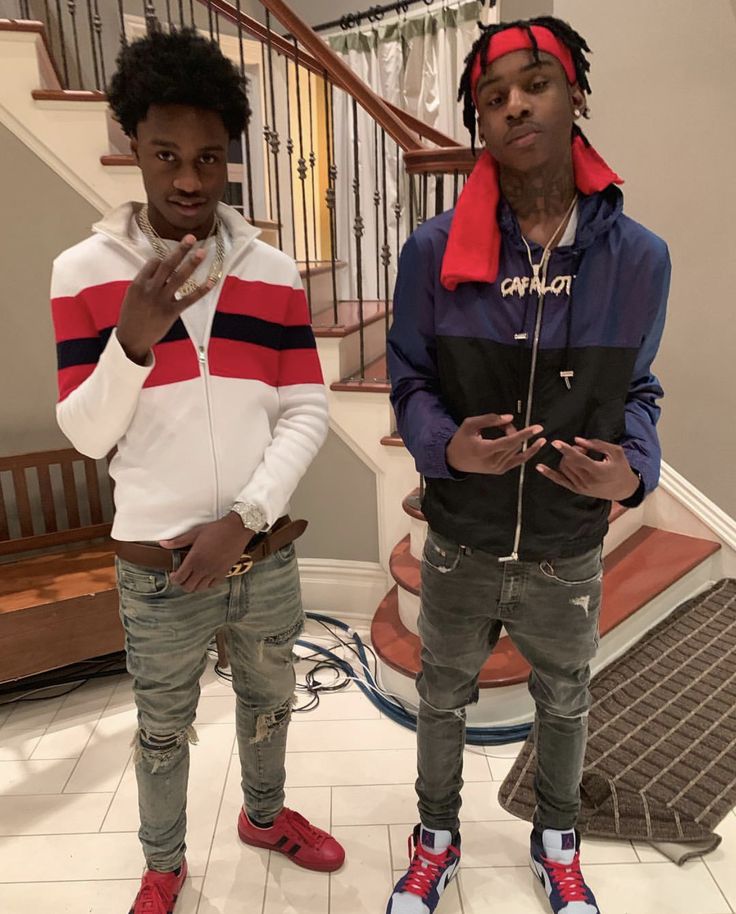 two young men standing next to each other in front of a stair case and looking at the camera