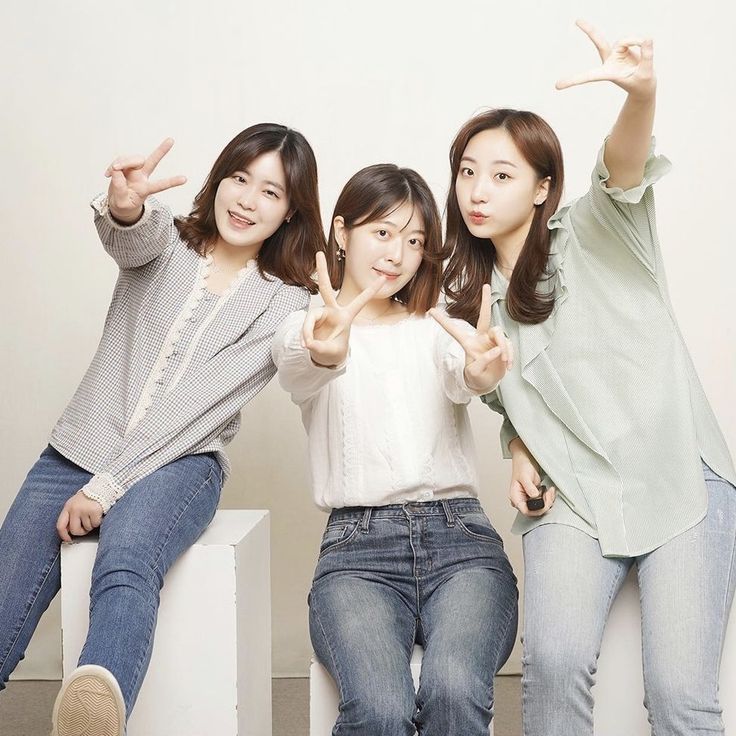 three young women sitting on top of white blocks making the peace sign with their hands