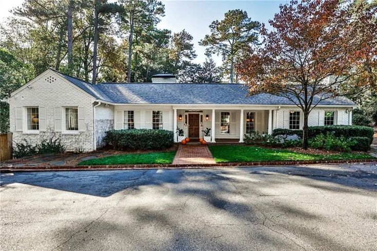 a white house in the middle of a street with lots of trees and bushes around it