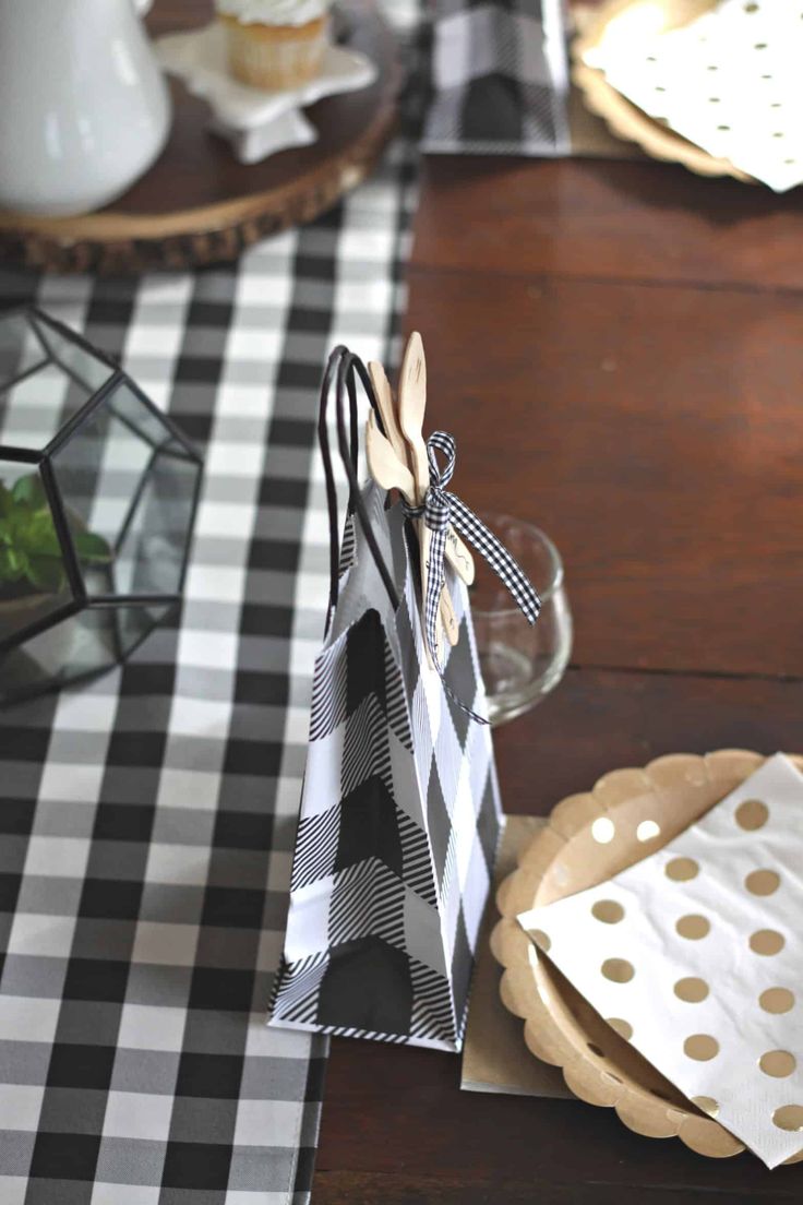 the table is set with black and white checkered napkins, gold polka dot paper bags, and cupcakes