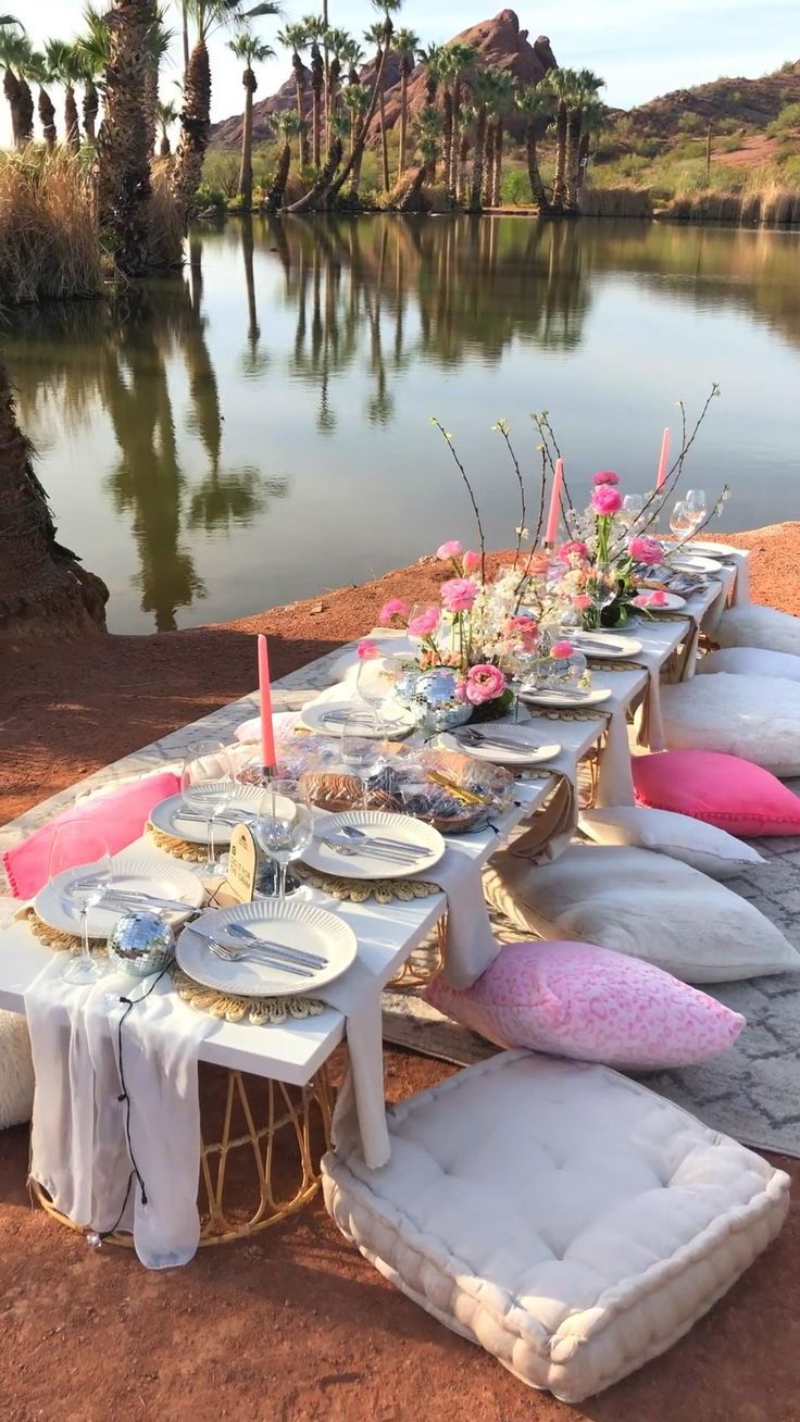 a long table set up with plates and place settings on the ground next to a body of water