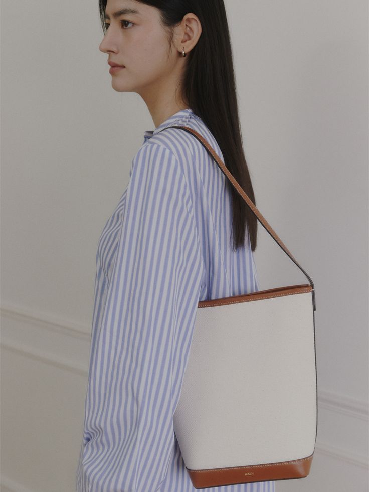 Editor's NoteROWH presents a timeless design that complements a variety of outfits.- Minimal bucket type bag- One handle, medium-sized shopper bag- Classic and spacious design- Inner open pocket detailMeasurements(in.)- Size: 10.24 in. * 10.83 in. * 4.72 in.- Strap: 10.24 in. Composition & Care- Upper: 100% Cotton, 100% Cow Leather / Lining: 65% Polyester, 35% Cotton / Strap: Cow Leather- Natural leather may have fine scratches and wrinkles- Bright leather can get stained by denim or da Workwear Bucket Hobo Bag With Detachable Handle, Chic Bucket-shape Shoulder Bag For Work, Workwear Bucket Hobo Bag, Structured Hobo Bag For Daily Use, Chic Bucket Bag For Work, Chic Bucket Bag For Workwear, Workwear Leather Handle Bucket Shoulder Bag, Workwear Bucket Shoulder Bag With Leather Handles, Everyday Structured Bucket Bag With Removable Pouch