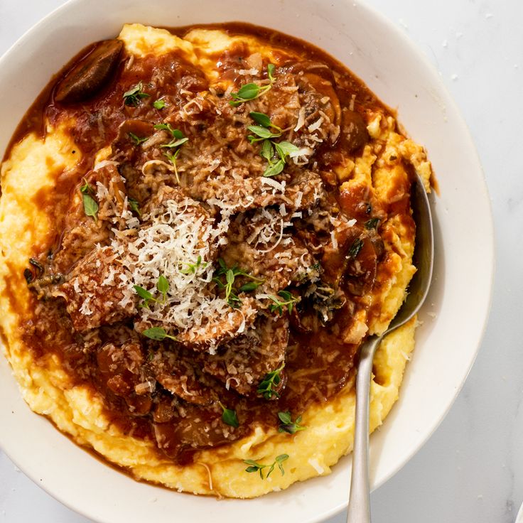 a white bowl filled with spaghetti and meat on top of mashed potatoes topped with parmesan cheese