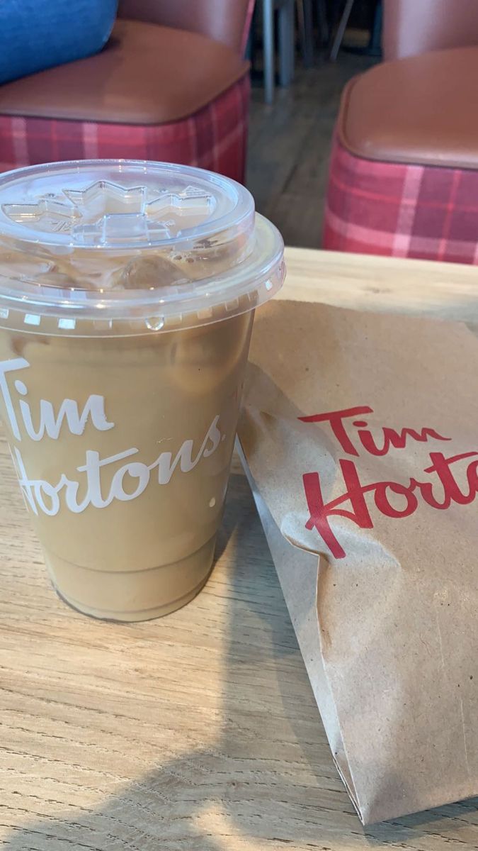 a cup of coffee sitting on top of a wooden table next to a paper bag