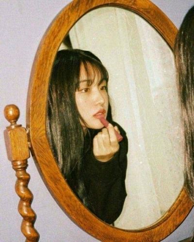 a young woman brushing her teeth in front of a mirror with the reflection of herself