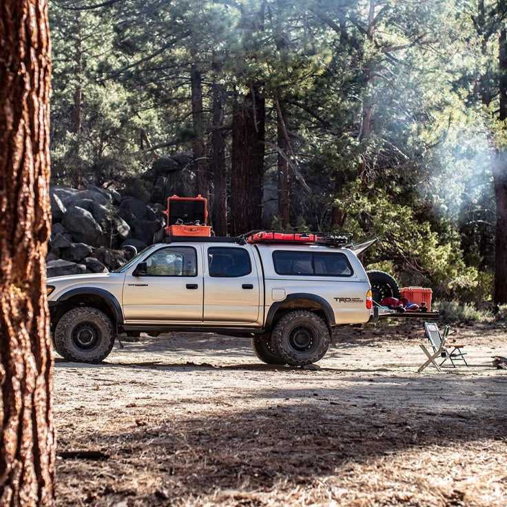 a pick up truck parked in the woods next to a camper with a tent on top