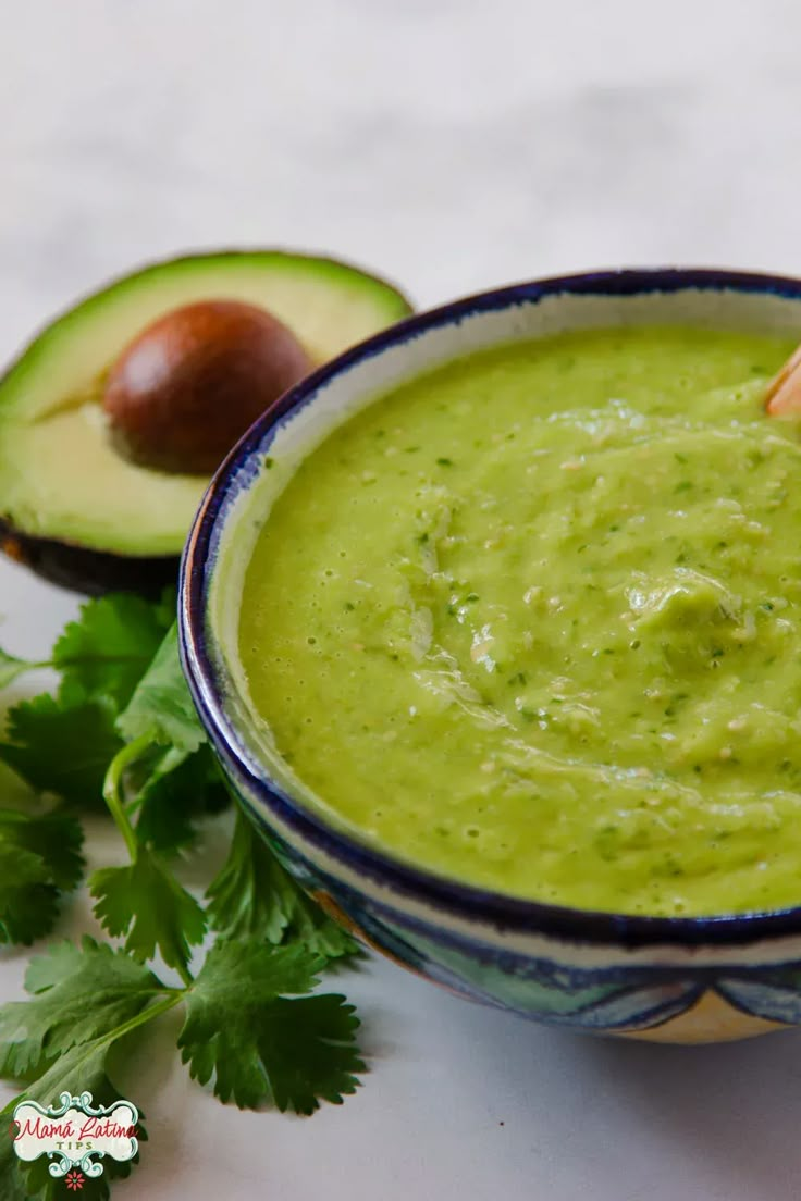 an avocado dip in a blue and white bowl next to some cilantro