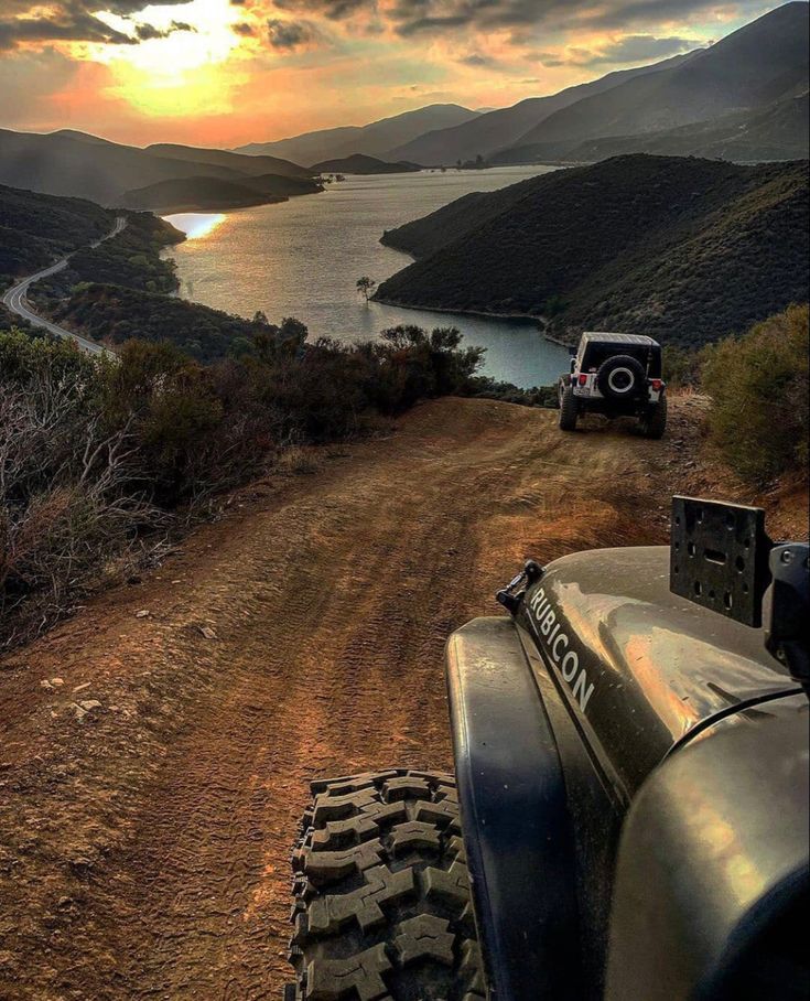 a jeep driving down a dirt road next to a body of water