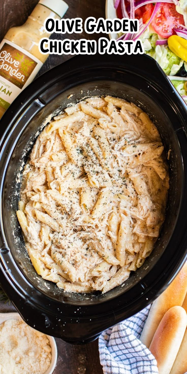 pasta in a crock pot with bread and salad behind it