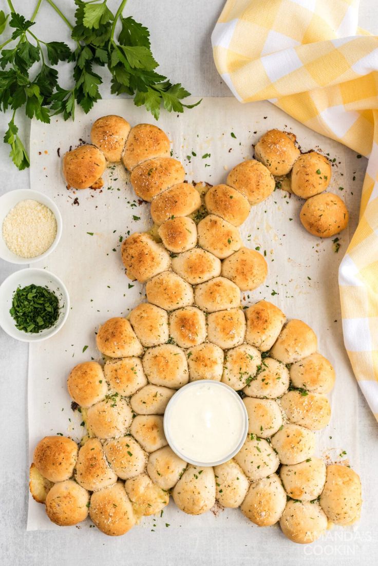 a table topped with rolls covered in cheese and parsley next to small bowls of dipping sauce