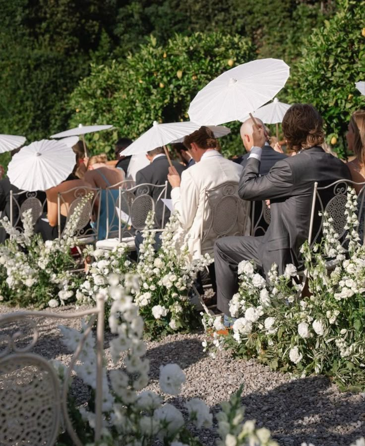 a group of people sitting under umbrellas in the sun at an outdoor wedding ceremony