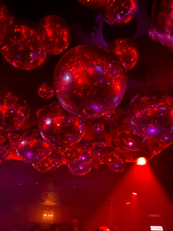 red and purple lights shine in the dark above people at a party with disco balls hanging from the ceiling