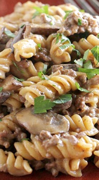 a red plate topped with pasta covered in meat and mushrooms, garnished with parsley