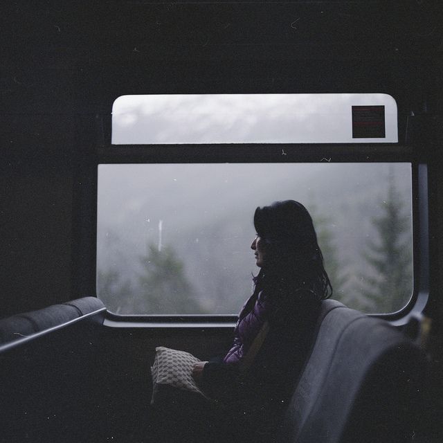 black and white photograph of woman sitting on train looking out the window at snow covered trees