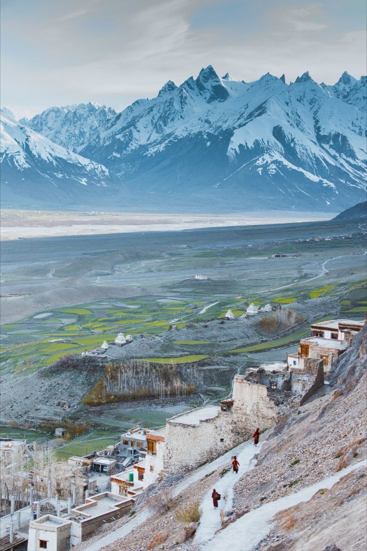 two people walking up the side of a snow covered mountain with mountains in the background