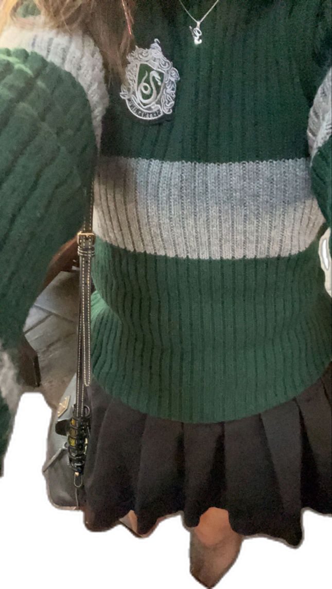 a woman wearing a green sweater and black skirt holding a cell phone in her hand