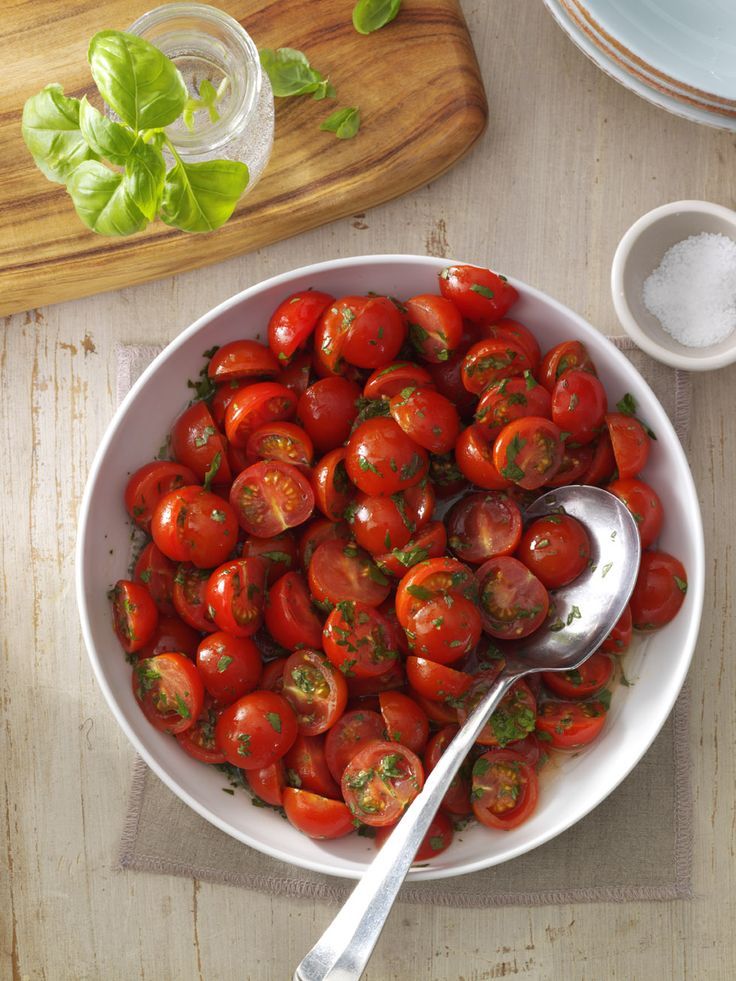 a white bowl filled with lots of cherry tomatoes next to a spoon and some seasoning