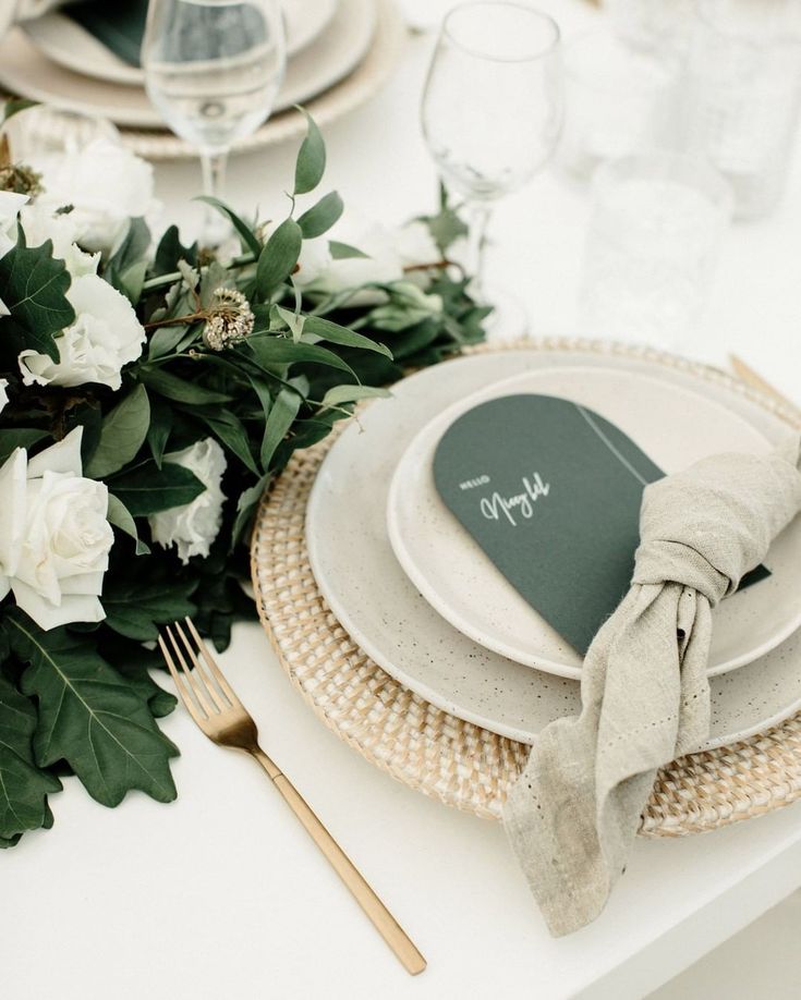 a place setting with white flowers and greenery